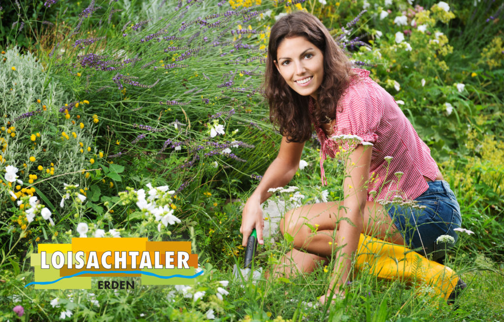 Lächelnde junge Frau bei der Gartenarbeit inmitten von Ziergräsern und Wildblumen, mit Loisachtaler Erden-Logo