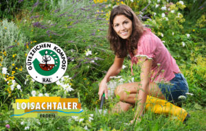 Lächelnde junge Frau bei der Gartenarbeit inmitten von Ziergräsern und Wildblumen, mit RAL Gütezeichen Kompost