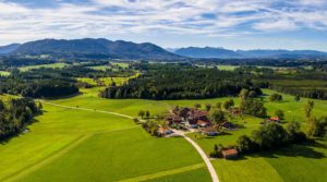 Sommerliches Luftbild des bayerischen Voralpenlandes mit großem Bauernhof und Gebirgspanorama